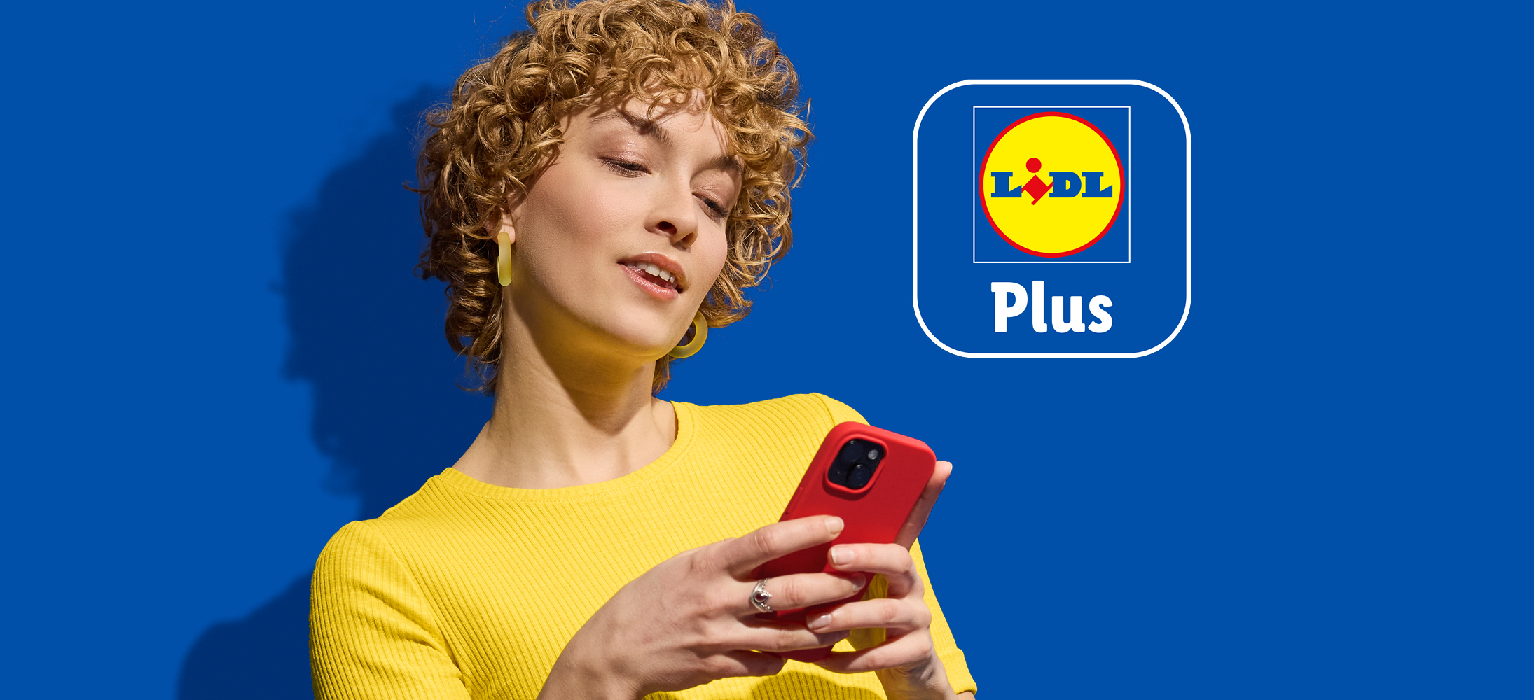Ženska z rdečim telefonom in logotipom Lidl Plus na modrem ozadju.