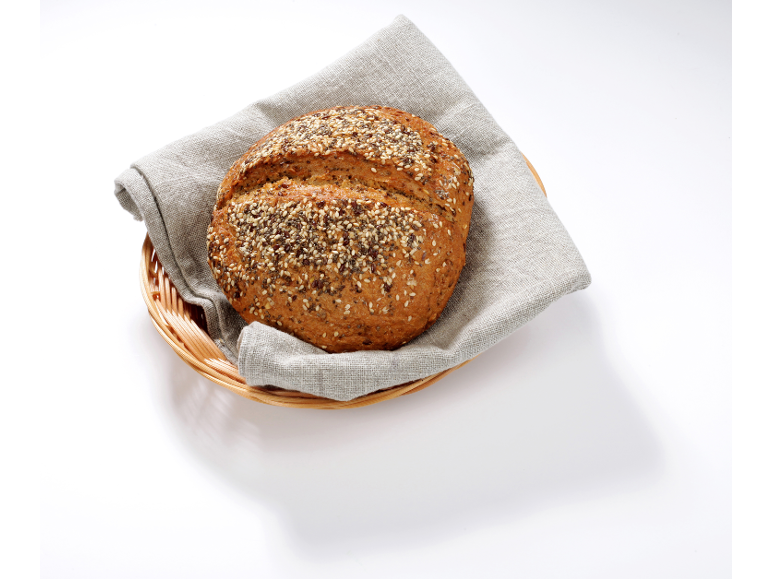 Okrogel polnozrnat kruh s semeni v košari s platneno krpo.