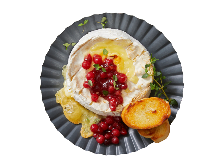 Pečen brie s brusnično omako, zelišči in toastom na sivem krožniku.
