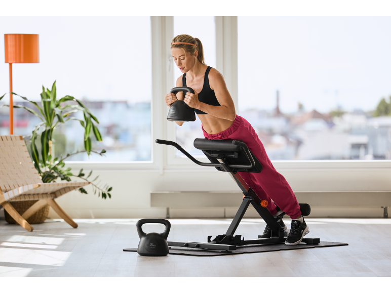 Ženska telovadi na fitnes klopi s črno utežjo v rokah.