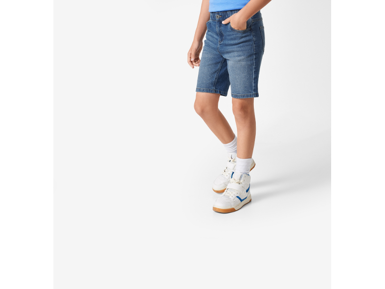 Deček v modrih jeans kratkih hlačah, modri majici in belih supergah z modrimi detajli.