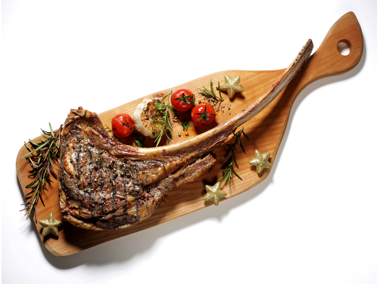 Tomahawk goveji zrezek s pečenim paradižnikom, česnom in rožmarinom na leseni deski.