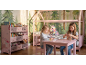 Dve deklici se igrata v rožnati otroški sobi z leseno posteljo in knjižno polico.