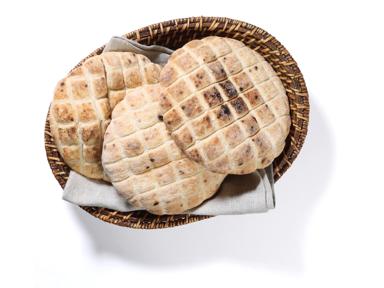Okrogel pita kruh z mrežastim vzorcem v pleteni košari s krpo.