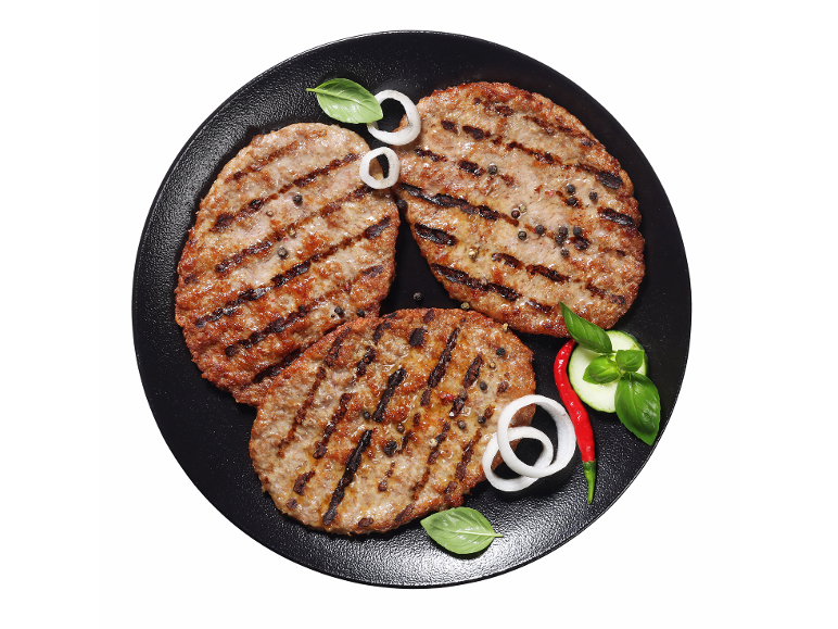 Žar burgerji s poprom, čebulo, baziliko, kumarami in čilijem na črnem krožniku.