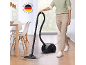 Ženska sesa tla s črnim sesalnikom, z oznako „Made in Germany“.