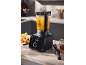 Črn kuhinjski mešalnik z oranžno juho, narezano zelenjavo in kozarcem tekočine.
