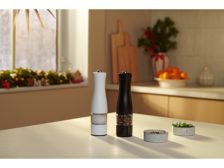 Črni in beli mlinčki za sol in poper na kuhinjski mizi z božičnimi okraski.
