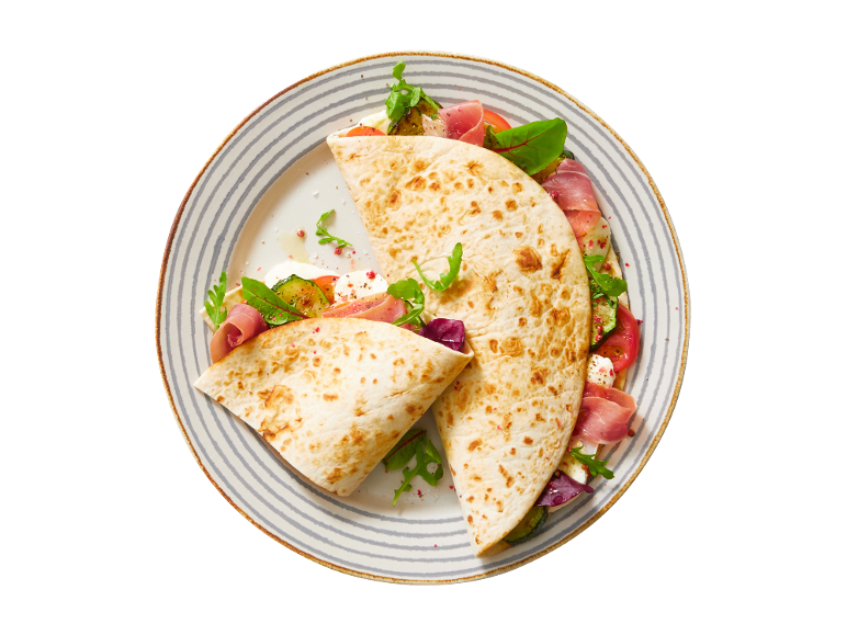 Piadina s pršutom, mocarelo, paradižnikom, bučkami in rukolo na črtastem krožniku.