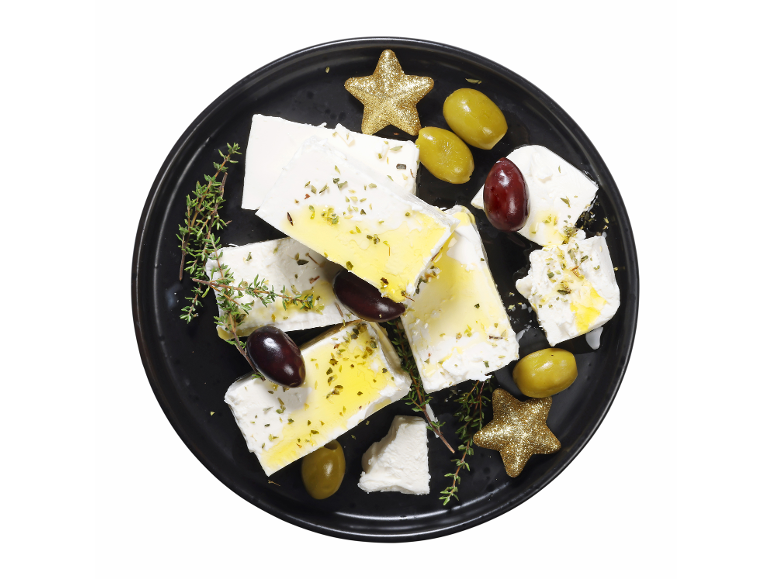 Feta sir z olivami, zelišči in oljčnim oljem na črnem krožniku, z zvezdnimi okraski.