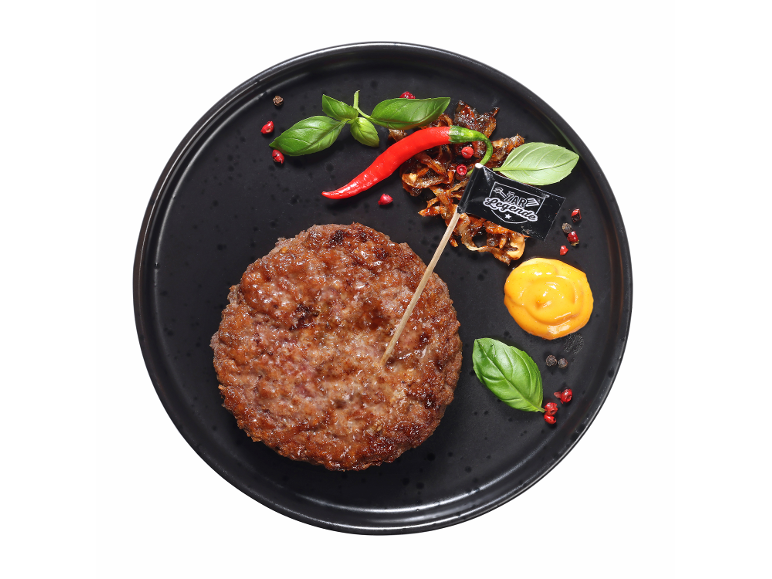 Mesni burger s čilijem, karamelizirano čebulo, baziliko in omako na črnem krožniku.