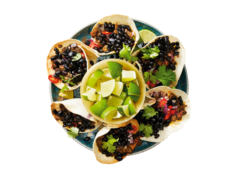 Tacos s črnim fižolom, mletim mesom, koriandrom in limeto na modrem krožniku.