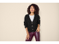 Ženska v črni pleteni jopici, beli majici in bordo usnjenih hlačah.