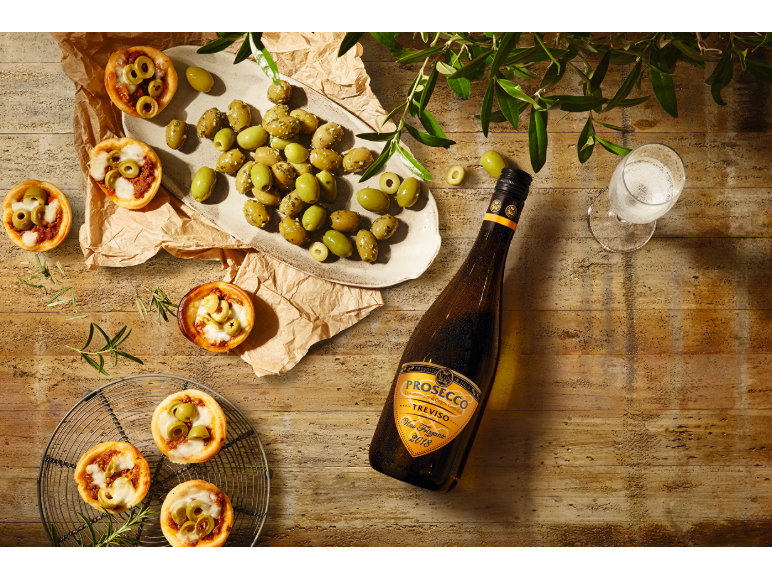 Mini pice in olive s steklenico Prosecca in kozarcem na leseni mizi.