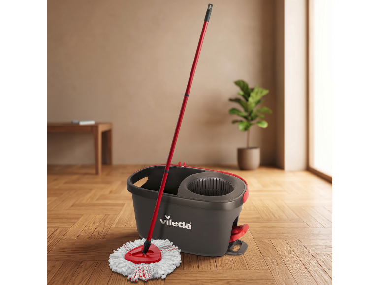 Rdeča krpa in siv vedro na tleh, v ozadju sobna rastlina.