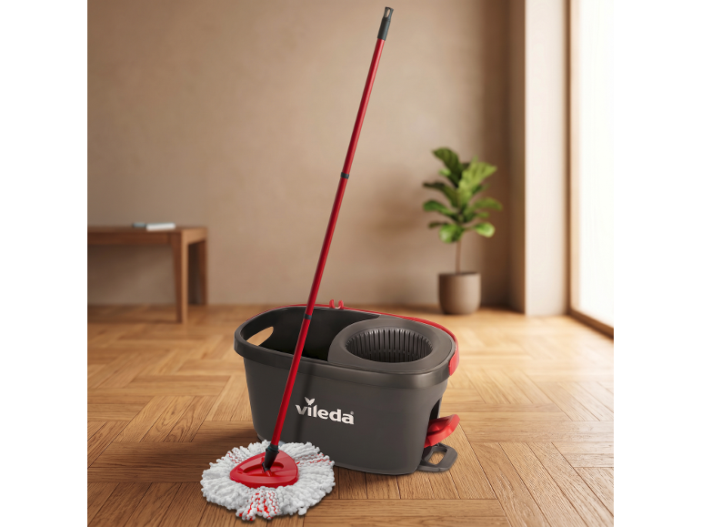 Rdeča krpa in siv vedro na tleh, v ozadju sobna rastlina.