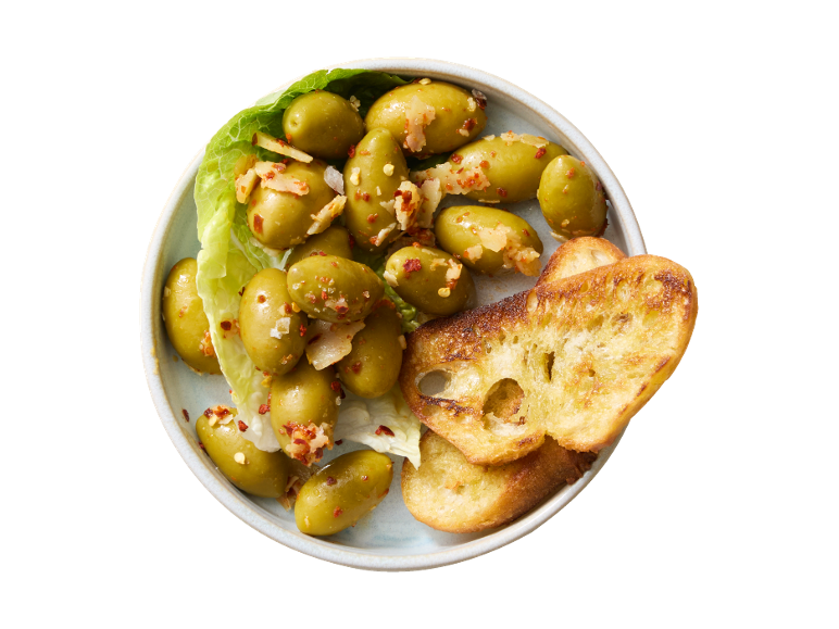 Marinirane zelene olive s čilijem in česnom, postrežene s popečenimi kruhki.