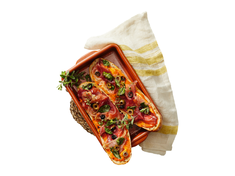 Bruschetta s pršutom, olivami in baziliko v keramični posodi.