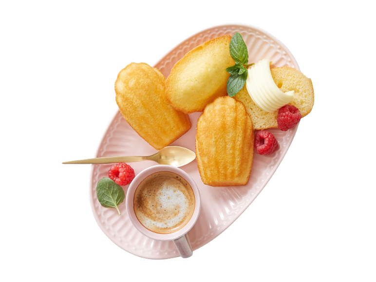 Madeleine, kava, maslo in maline na rožnatem krožniku.