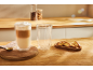 Latte macchiato v kozarcu z dvojno steno in piškoti na leseni kuhinjski površini.