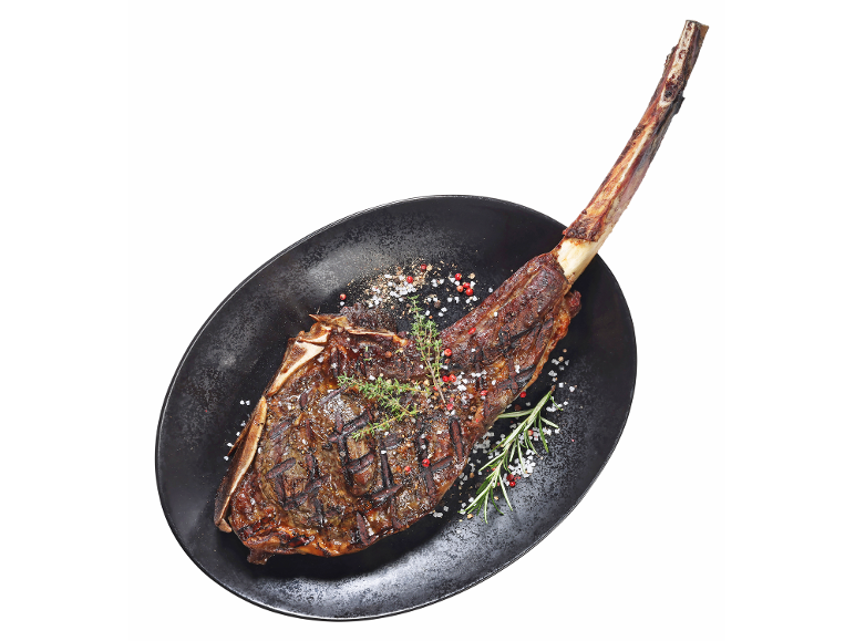 Pečen goveji tomahawk z zelišči in začimbami na črnem krožniku.