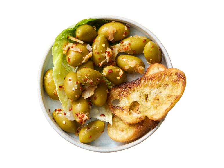 Marinirane zelene olive s čilijem in česnom, postrežene s popečenimi kruhki.