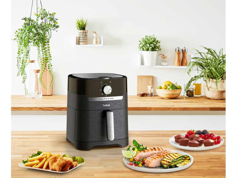 Tefal Easy Fry & Grill cvrtnik na vroč zrak na kuhinjskem pultu s pripravljeno hrano.