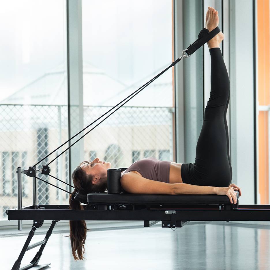 Ženska izvaja vajo za noge na pilates reformer napravi.