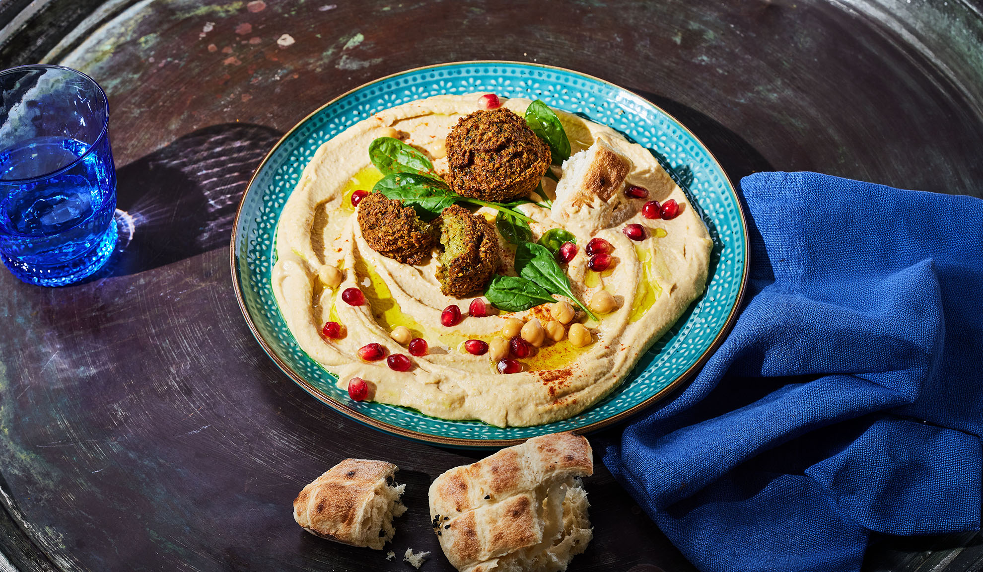Humus s falafli, semeni granatnega jabolka in pita kruhom na temni mizi.