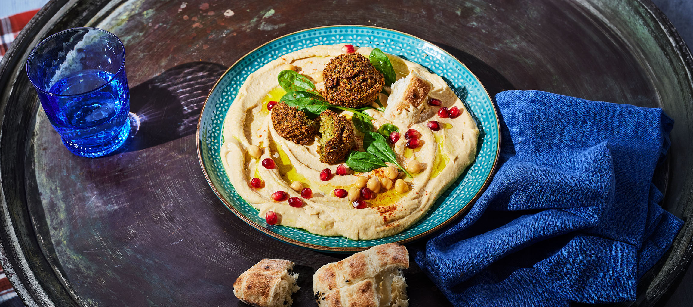 Humus s falafli, semeni granatnega jabolka in kruhom na kovinskem pladnju.