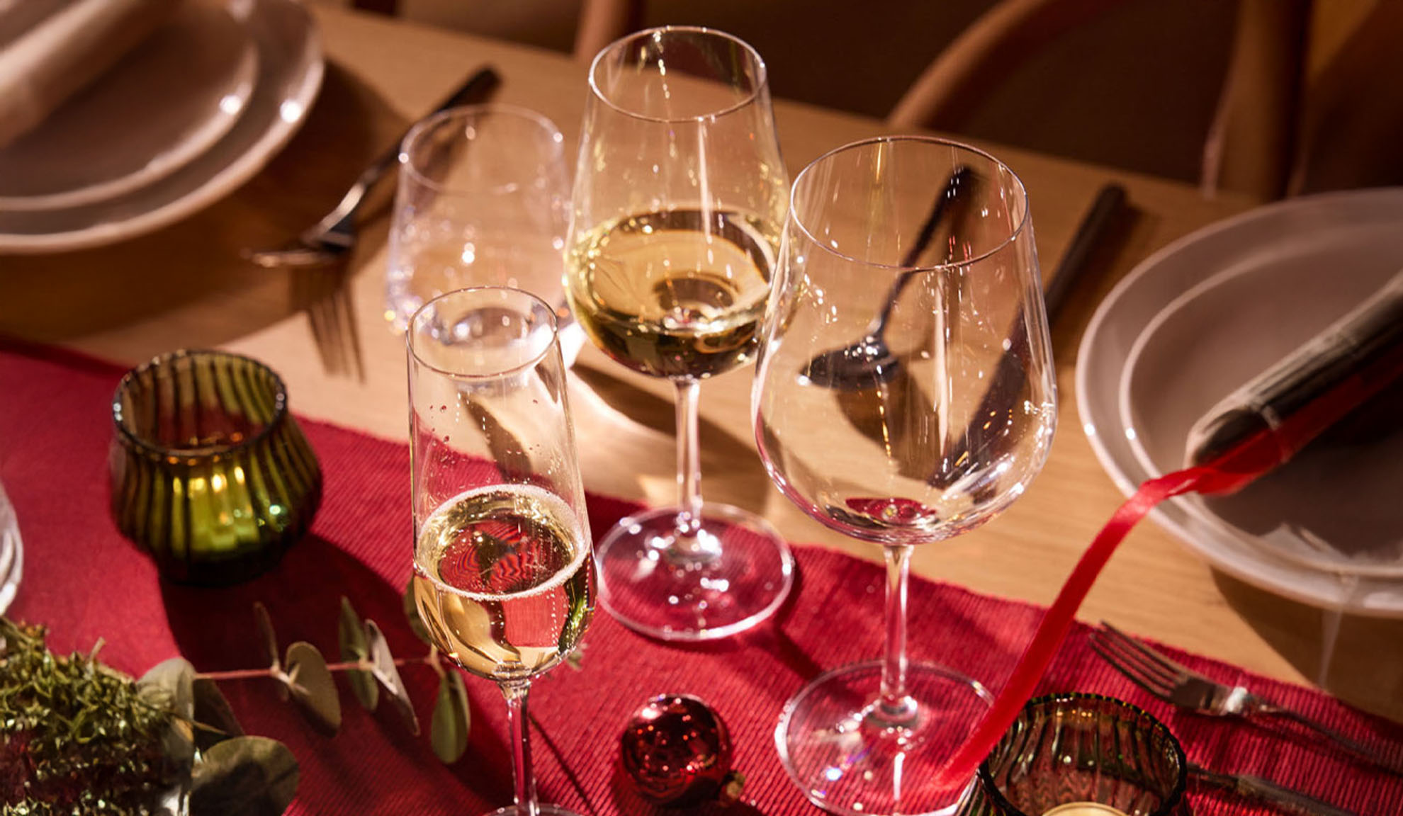 Praznično pogrnjena miza z vinskimi kozarci, kozarcem za šampanjec in božičnimi okraski.