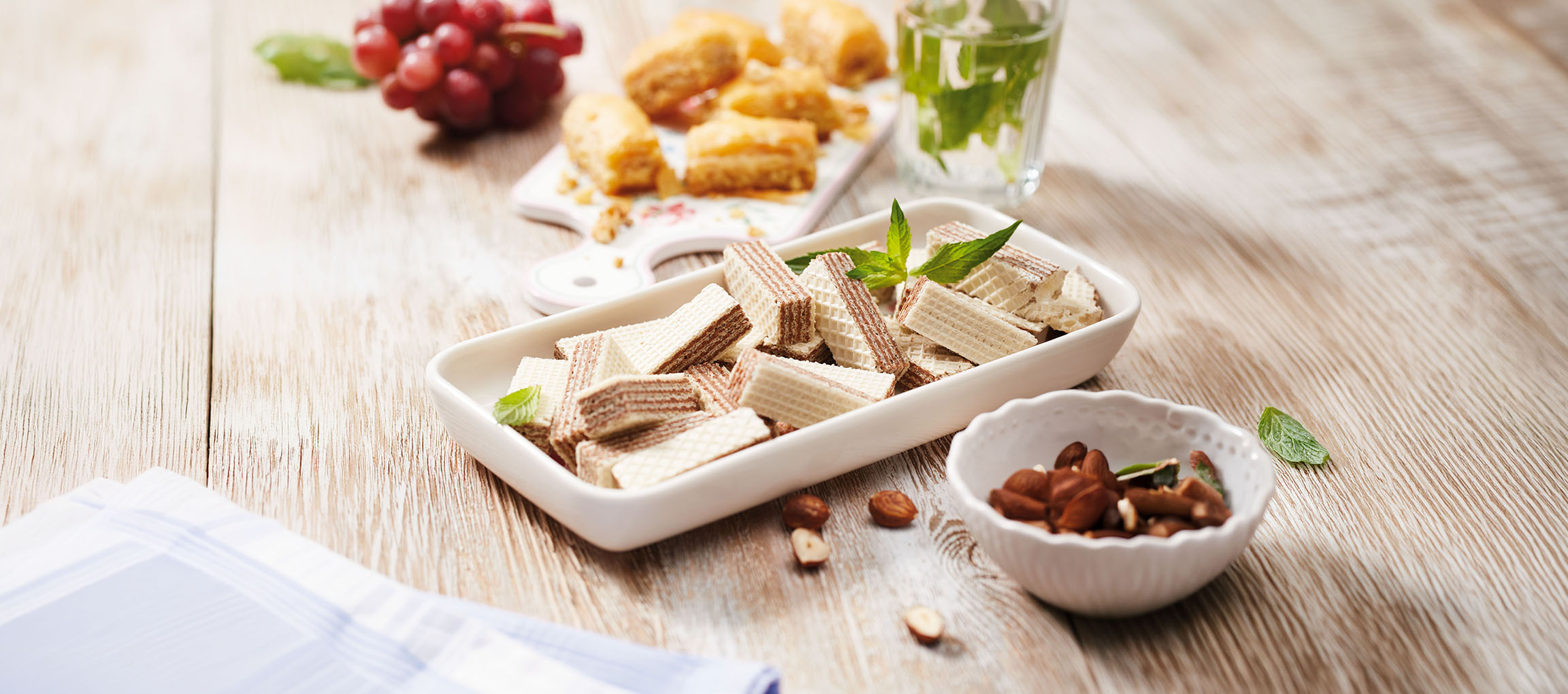 Vaflji, baklava, grozdje in meta voda na leseni mizi.