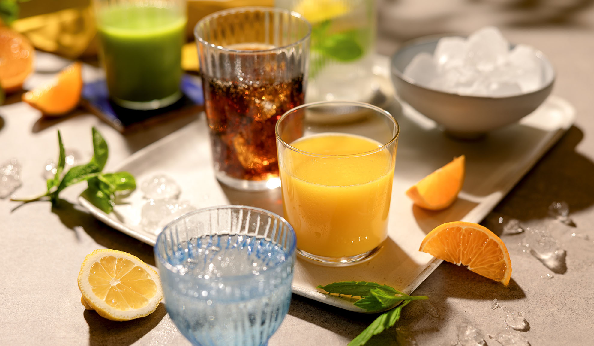 Različne osvežilne pijače z ledom, rezinami citrusov in meto na pladnju.