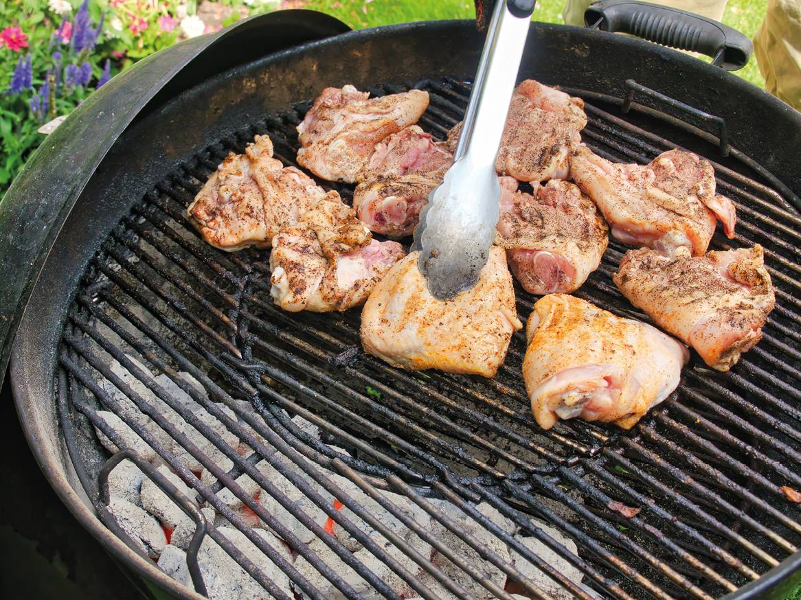 Piščančja bedra na žaru s kleščami, ki obračajo en kos.