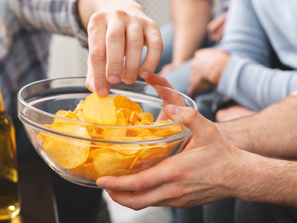 Moški si postreže s čipsom iz sklede, medtem ko drugi drži skledo.