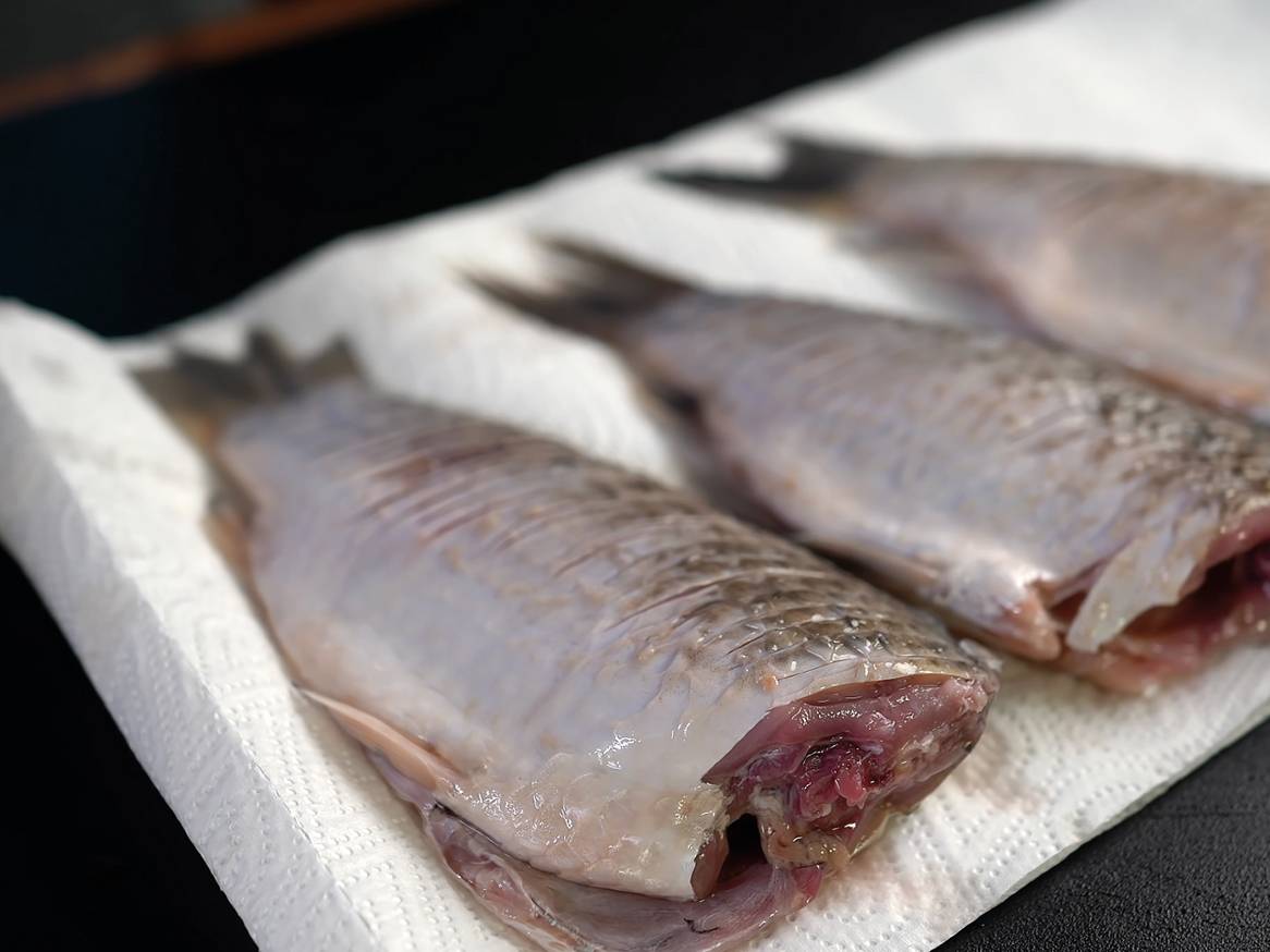 Tri očiščene ribe, pripravljene za kuhanje, ležijo na beli papirnati brisači.