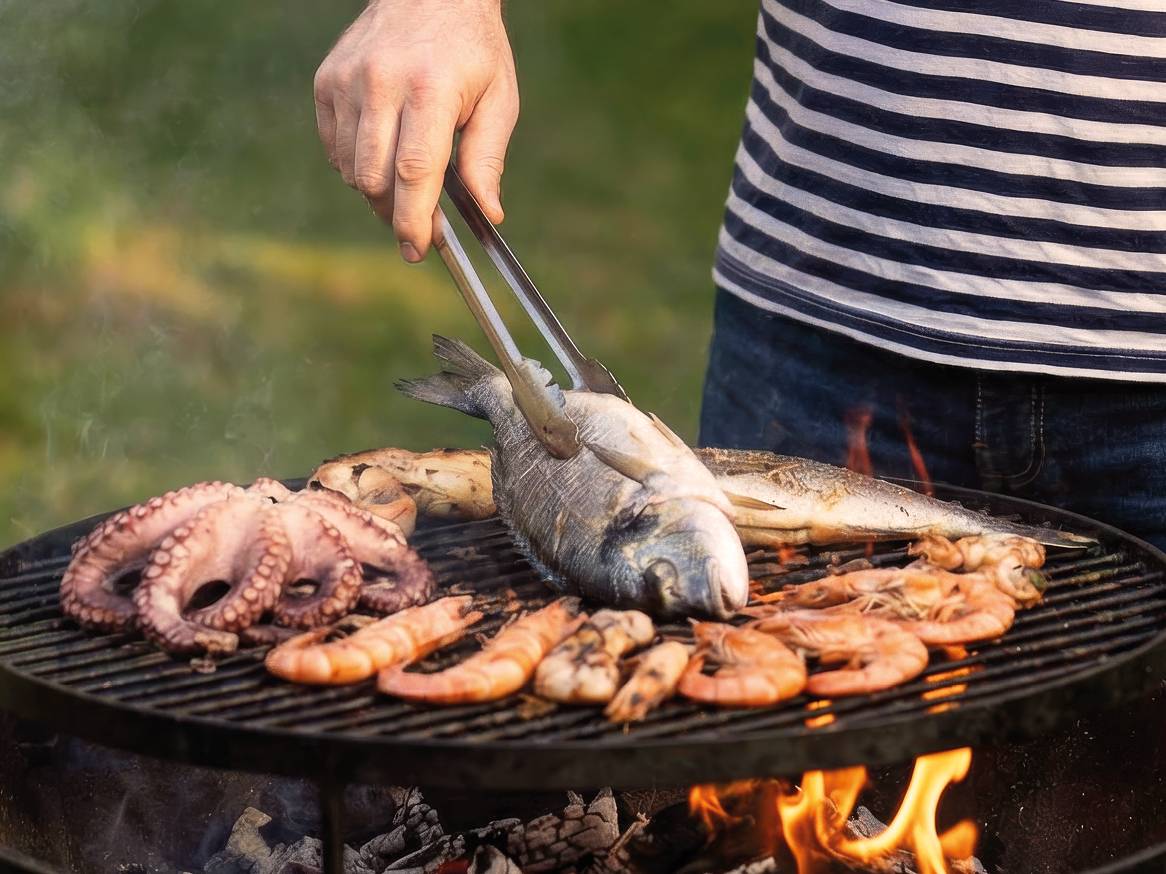 Moški peče ribe, hobotnico in kozice na žaru na prostem.