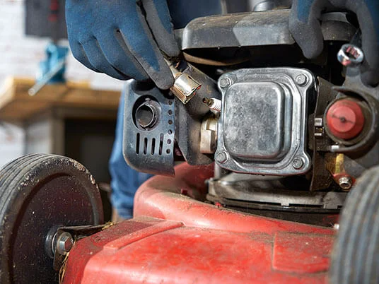 Roke v rokavicah menjajo svečko na rdeči kosilnici.