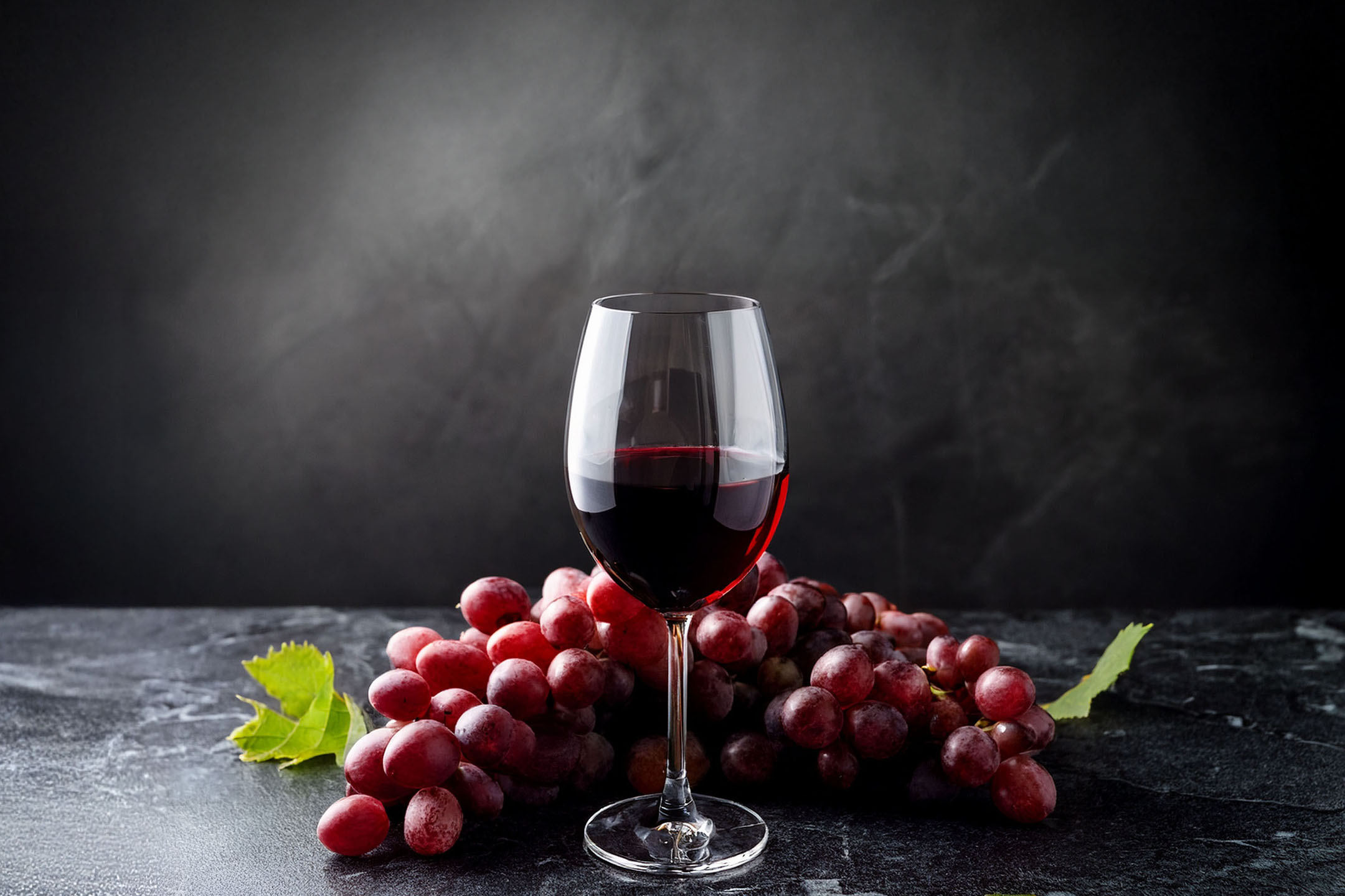 Kozarec rdečega vina in grozd rdečega grozdja na temnem ozadju.