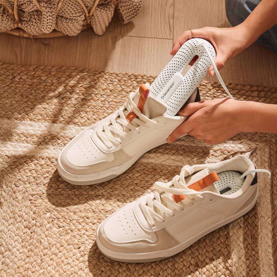 Sušilec čevljev Silvercrest v belih supergah na pleteni preprogi.