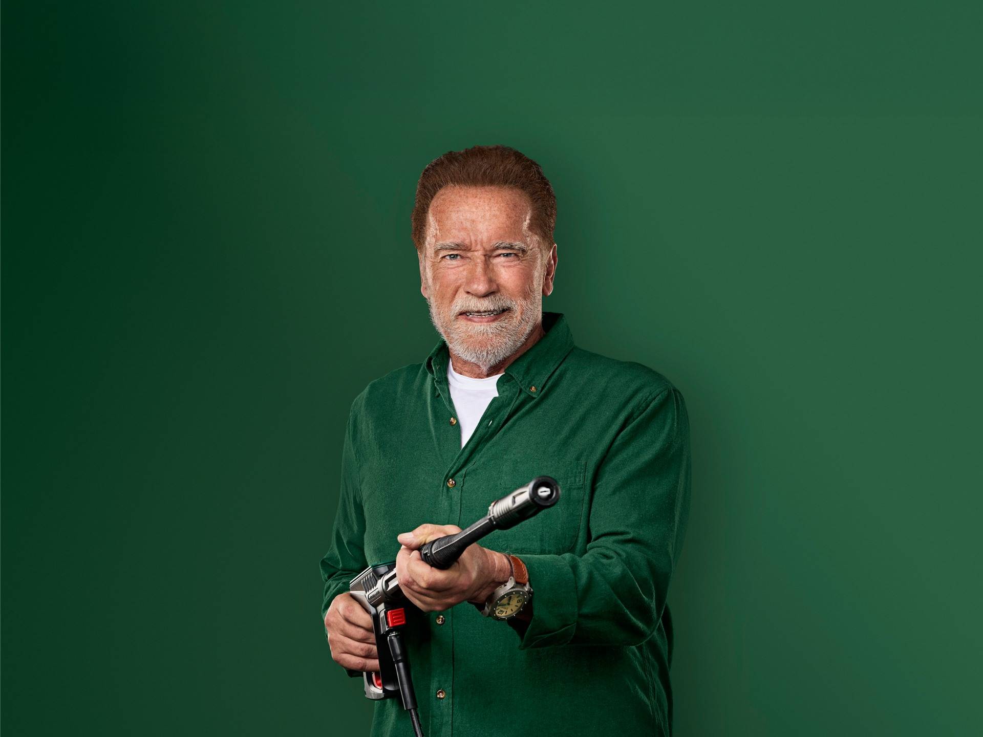Arnold Schwarzenegger se smehlja, drži pištolo za visokotlačni čistilec.