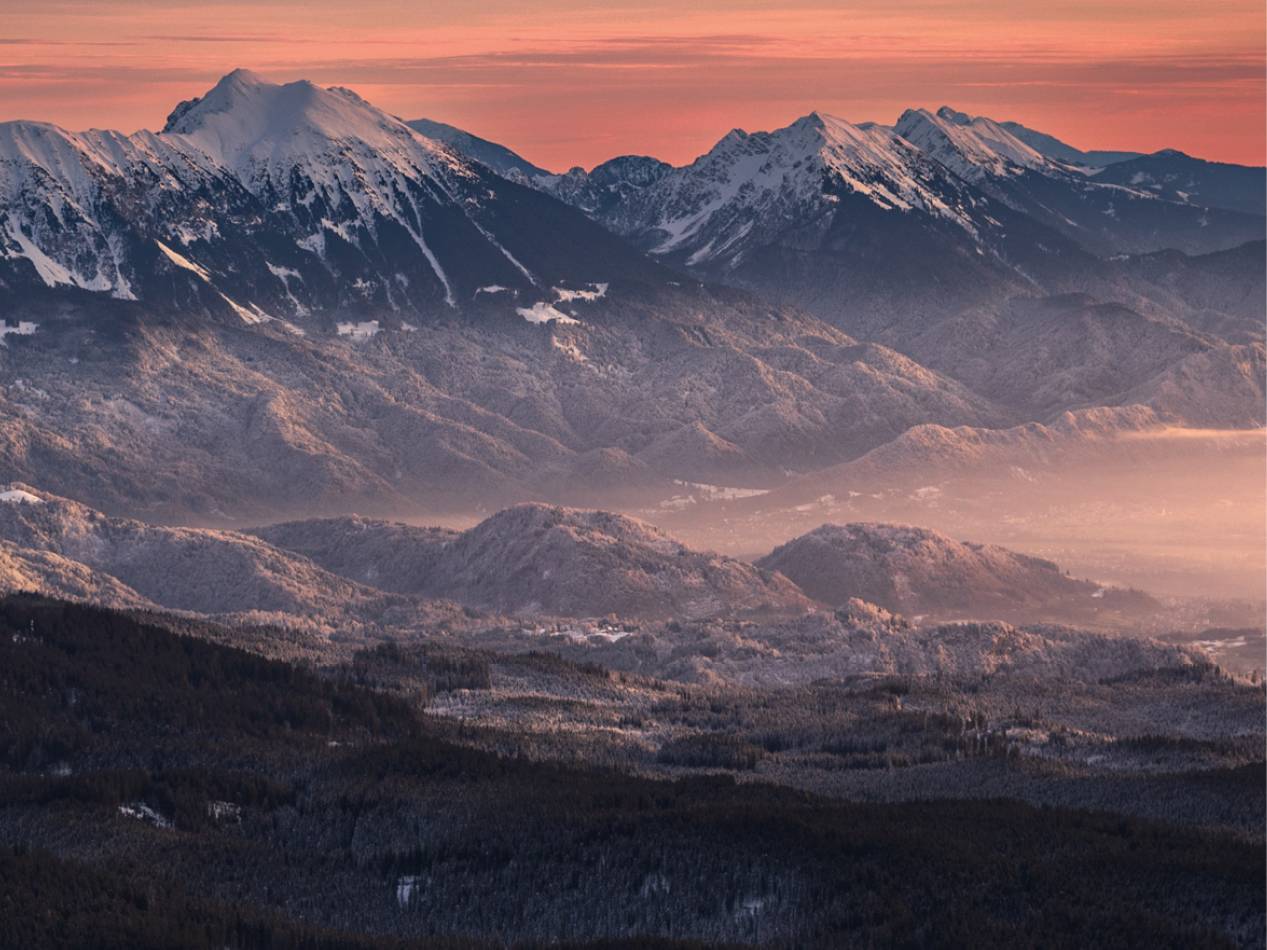 Zasnežene gore in gozdovi ob sončnem zahodu.