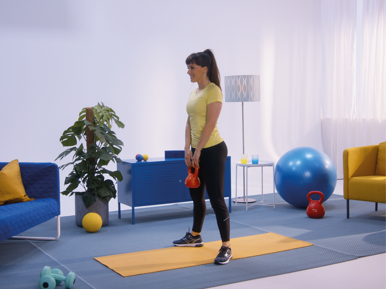 Ženska v telovadni opremi drži utež kettlebell v sobi z vadbeno opremo.
