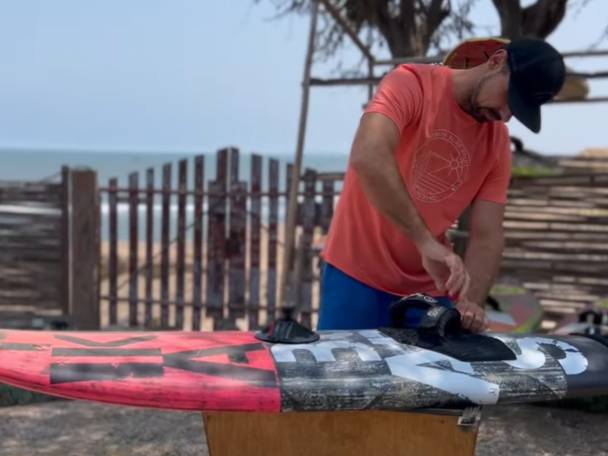 Moški pritrjuje vezalke na desko za kajtanje na plaži.