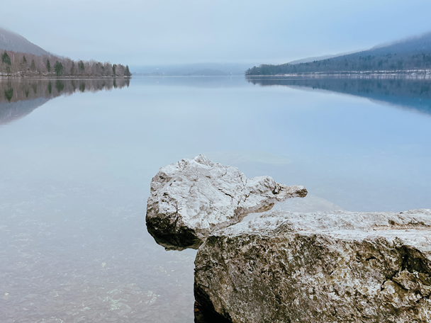 Mirno jezero z odsevi dreves in skal v ospredju.
