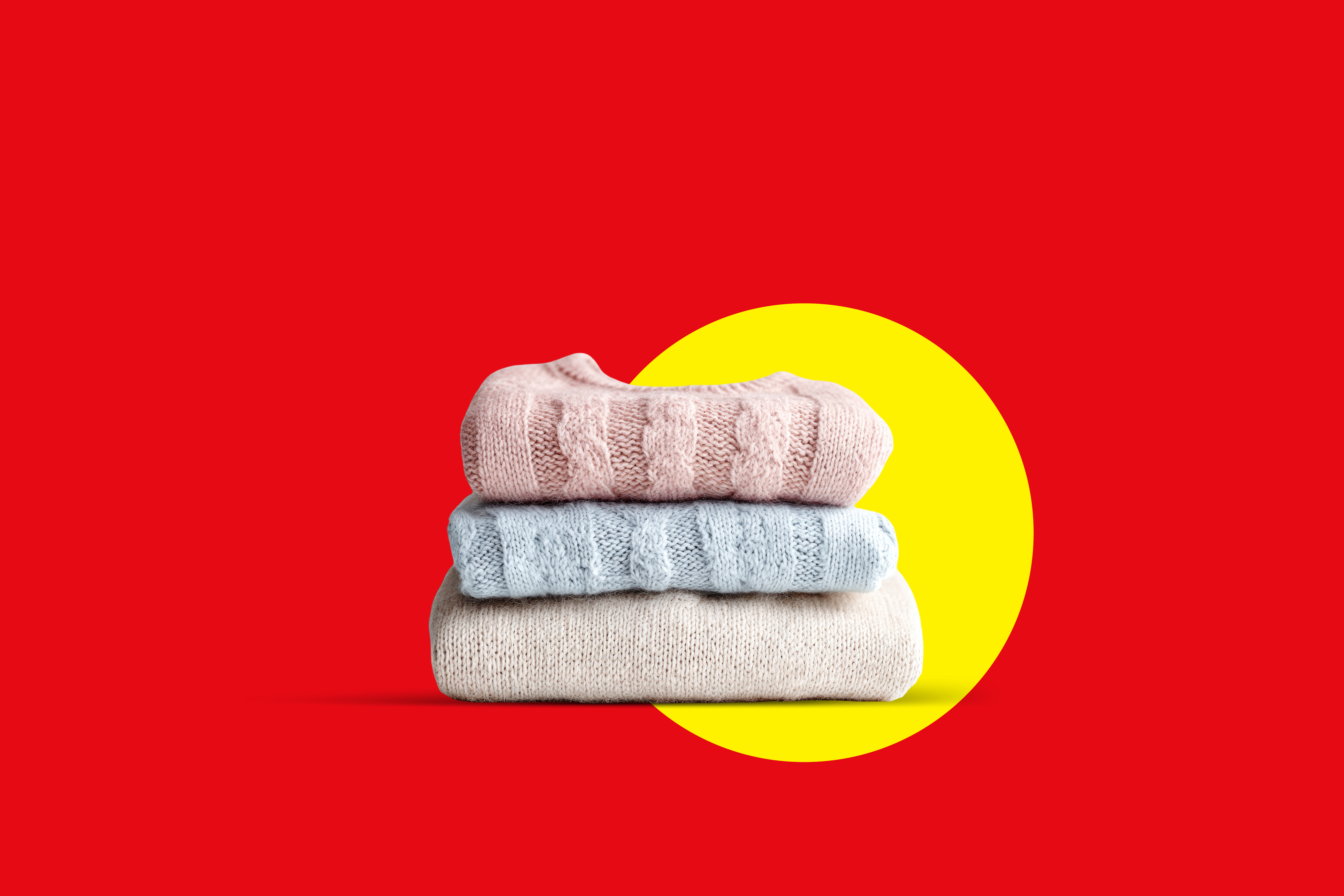 Kup zloženih pletenin v roza, modri in bež barvi na rdečem ozadju z rumenim krogom.