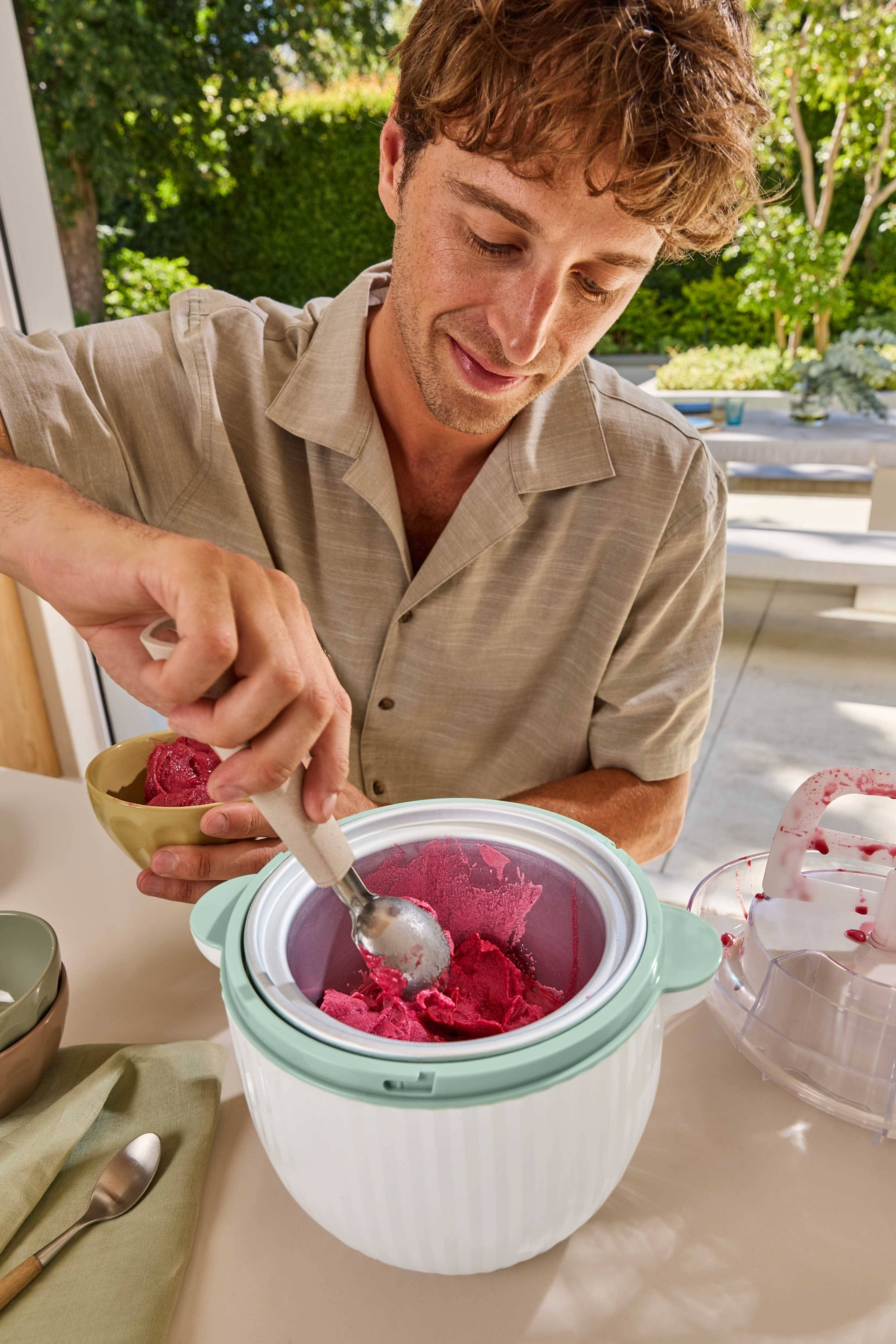 Moški zajema rdeč sorbet iz aparata za sladoled v skledo.