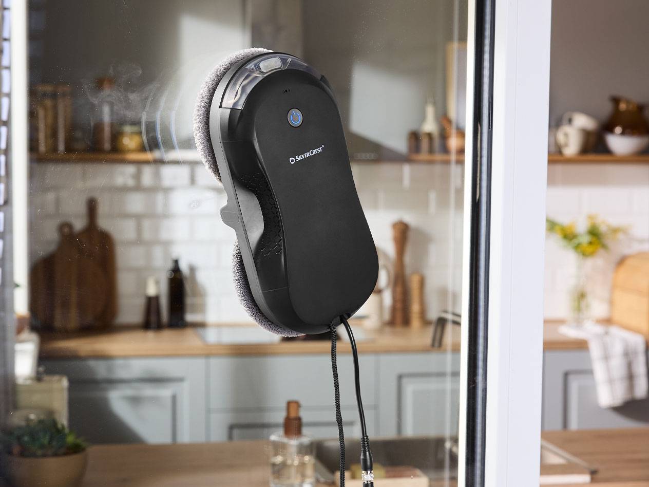 Silvercrest robot za čiščenje oken na oknu s kuhinjo v ozadju.