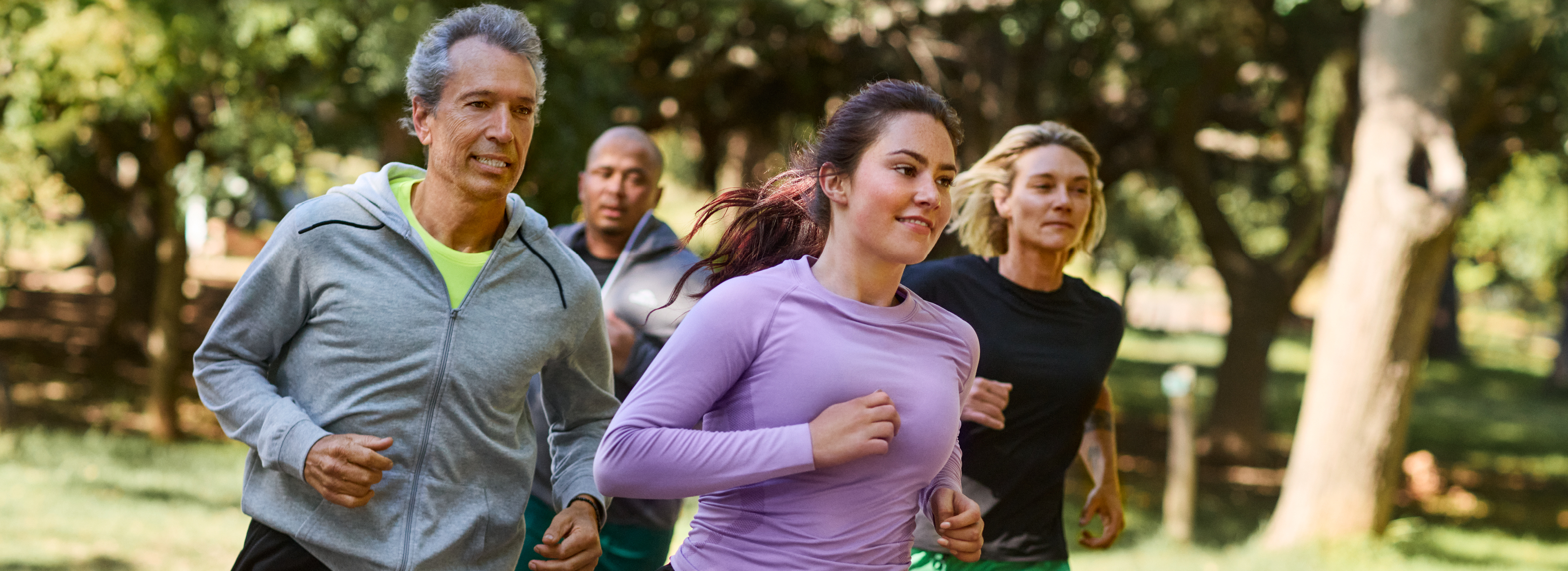 Štirje tekači v športnih oblačilih, v ospredju ženska v vijolični majici in črnih kratkih hlačah.