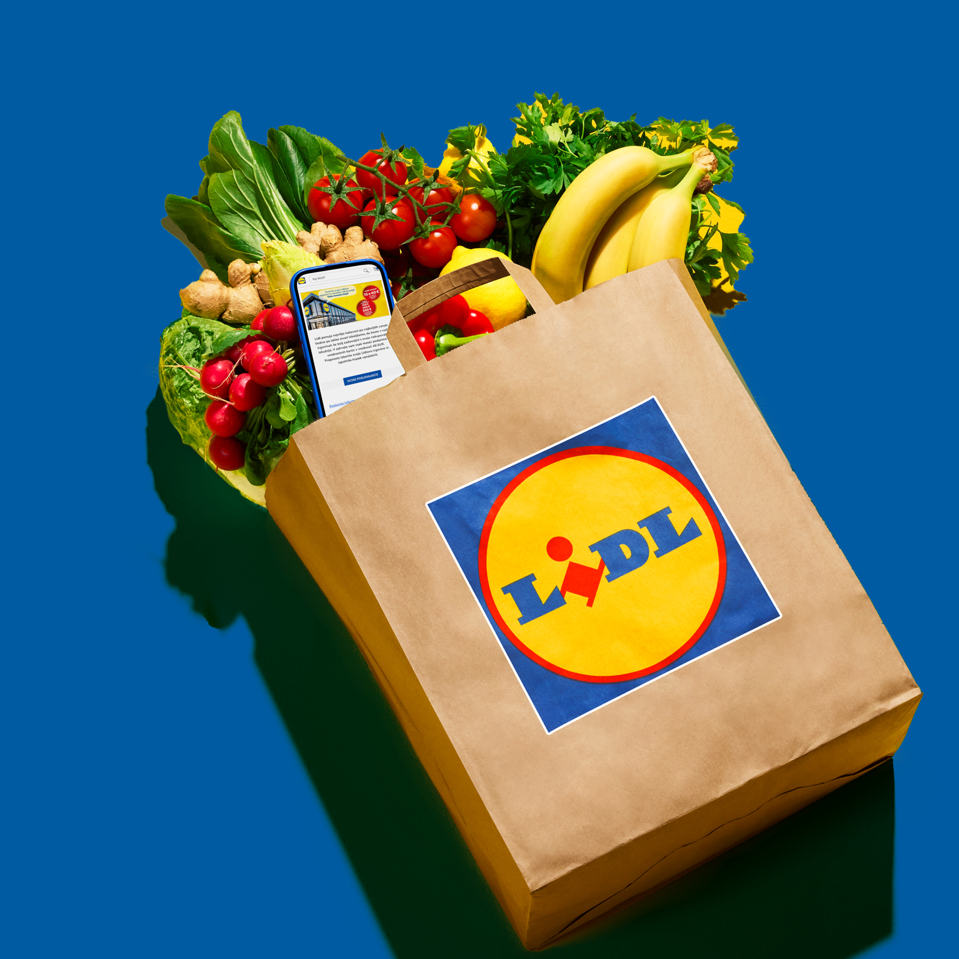 Nakupovalna vrečka Lidl, polna sveže zelenjave, sadja in pametnega telefona z aplikacijo Lidl.